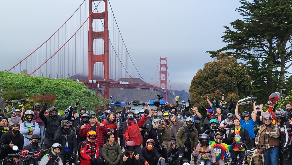 Dozens of helmeted riders at the Golden Gate Bridge, wheels held overhead.